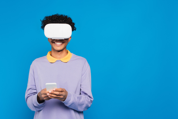 cheerful african american man using smartphone in vr headset isolated on blue - Fotoğraf, Görsel