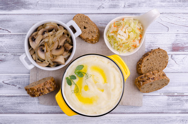 Bramborová kaše s máslem, smažené houby s cibulí a salátem z čerstvé zeleniny na světlém dřevěném pozadí. Selektivní zaměření. - Fotografie, Obrázek