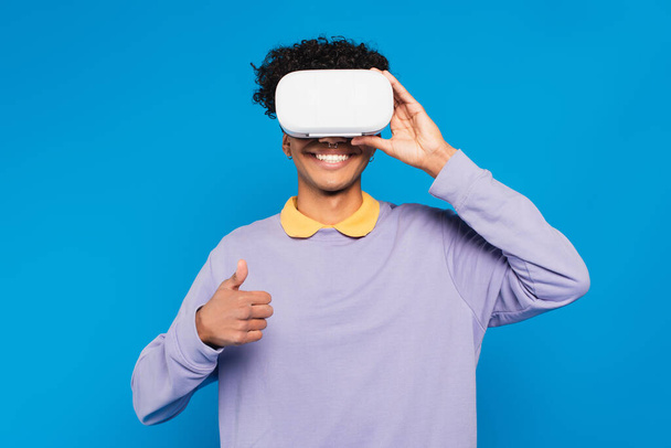happy african american man in lilac jumper and vr headset showing thumb up isolated on blue - Photo, image