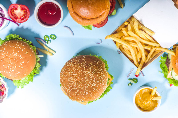 Fastfood, hamburgerparty concept. Diverse heerlijke hamburgers set met frietjes en sauzen op helderblauwe achtergrond flatlay bovenaanzicht kopieerruimte - Foto, afbeelding