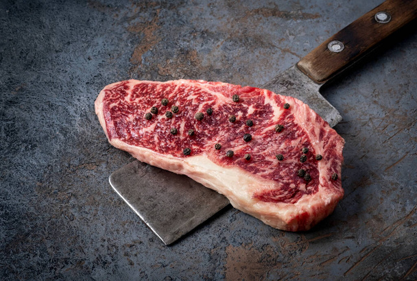 Saftiges Raw New Strip Steak und ein Schlachterbeil in Nahaufnahme auf dunklem Hintergrund - Foto, Bild