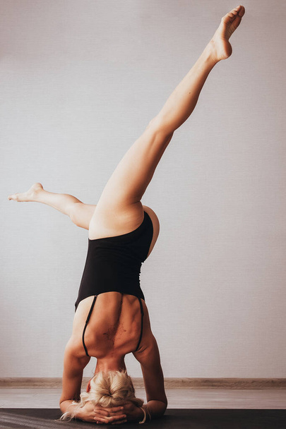 Een mooie blondine in een sportbadpak doet aan yoga, oefent verschillende asanas op de mat - Foto, afbeelding