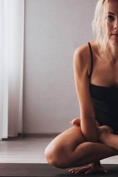 Een meisje in een sportbadpak doet aan yoga - ze tilt haar lichaam boven de mat, haar benen in een lotus - Foto, afbeelding