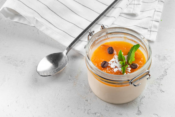 Panna cotta dessert met sinaasappelgelei en munt in een glazen pot op een keuken - Foto, afbeelding