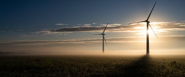 Two wind turbines in the early morning fog at sunrise in the English countryside panoramic - Φωτογραφία, εικόνα