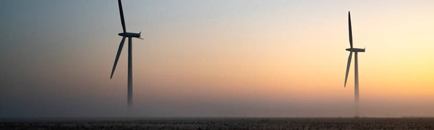 Two wind turbines in the early morning fog at sunrise in the English countryside panoramic - Foto, imagen