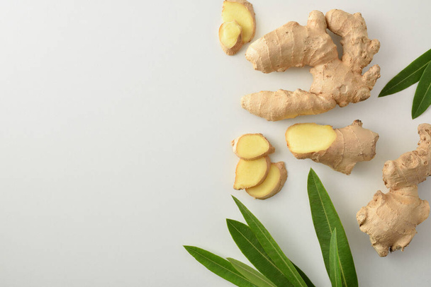 Ginger root with sliced portions and leaves on white table. Top view. - Foto, afbeelding