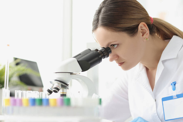 Μια λευκή γυναίκα χημικός που κοιτάζει το μικροσκόπιο. - Φωτογραφία, εικόνα