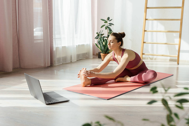 Attractive young woman doing stretching online at home under guidance of professional trainer online. Self-isolation and social distance during covid pandemic. Health care, life balance concept  - Photo, Image