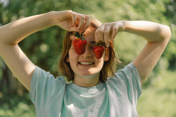 Young Teenager Girl with strawberry in a t-shirt in a outdoor and looking at camera. People and lifestyle concept - Photo, Image