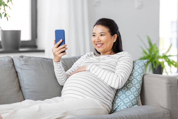 happy pregnant woman with smartphone at home - Foto, afbeelding