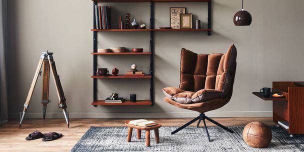 Stylish interior of living room with design brown armchair, wooden bookcase, pendant lamp, carpet decor, picture frames and elegant personal accessories in modern retro home decor. Template. - Photo, image
