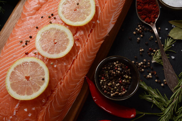 Fresh raw salmon fish fillet with spices and lemon slices over dark stone background - Fotó, kép