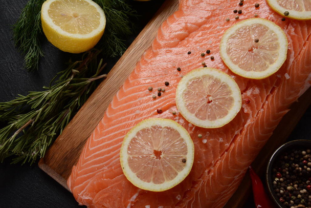 Fresh raw salmon fish fillet with spices and lemon slices over dark stone background - Fotó, kép
