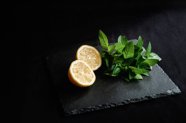 Ingrediënten voor mojito zomer citruscocktail met citroen en munt. Pepermunt met citrusvruchten op een zwart bord voor het serveren - Foto, afbeelding