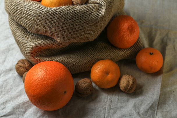 Ripe, tasty and juicy oranges, tangerines in a canvas bag with walnuts on the table. - Foto, afbeelding