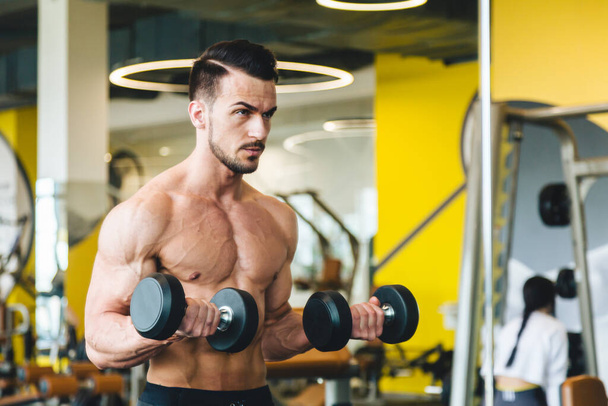 athletic man doing dumbbell exercise in front of a mirror bare torso in the gym - Foto, immagini