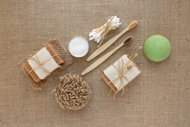 Set of different natural bathroom tools, sustainable lifestyle and zero waste concept. Wooden toothbrushes, bamboo swabs, soap, toothpowder and sponge konjac on fabric background with copy space - Фото, изображение