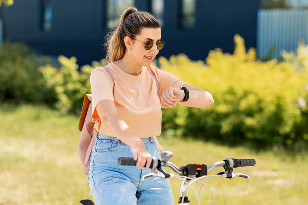 woman with smart watch riding bicycle in city - Фото, изображение