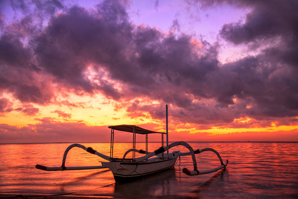 Bela paisagem do nascer do sol com Jukung é barcos de pesca balineses tradicionais em Karang Beach, Sanur, Bali, Indonésia.Barco de pesca na praia do mar com fundo do nascer do sol. - Foto, Imagem