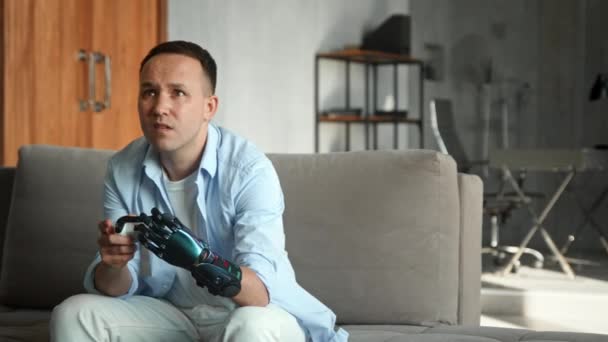 Hombre serio con mano artificial de alta tecnología juega juego de consola - Metraje, vídeo
