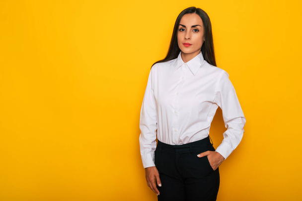 Modern happy successful confident business woman in a white shirt is posing on yellow background - Foto, imagen
