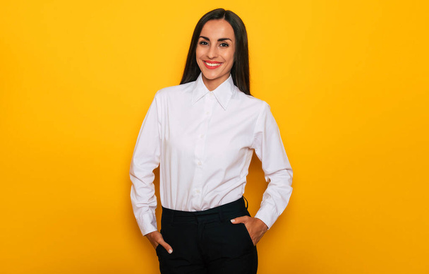 Σύγχρονη ευτυχισμένη επιτυχημένη επιχειρηματίας με αυτοπεποίθηση σε λευκό πουκάμισο ποζάρει σε κίτρινο φόντο - Φωτογραφία, εικόνα