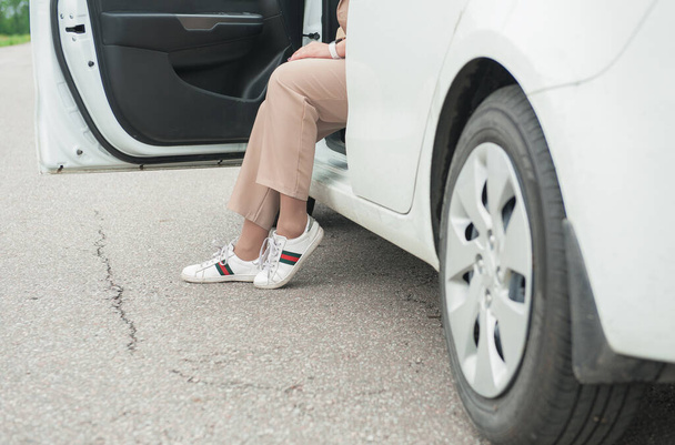 Legs of woman with sneakers out of white car on the road outdoor - Fotoğraf, Görsel