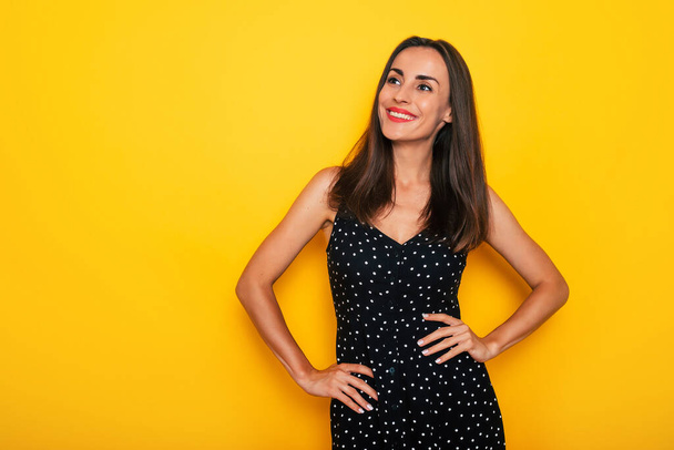 Happy excited gorgeous smiling brunette woman in a black summer dress is posing isolated on yellow background and having fun - 写真・画像