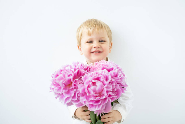 child blonde boy with big bouquet of pink peonies on white background. Love and romantic concept. - Foto, imagen
