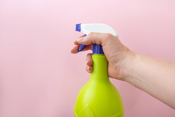 Käsi tilalla muovi spray keltainen pullo eristetty vaaleanpunainen tausta. Pullo pesuainetta tai kasvien suihkutusta varten - Valokuva, kuva