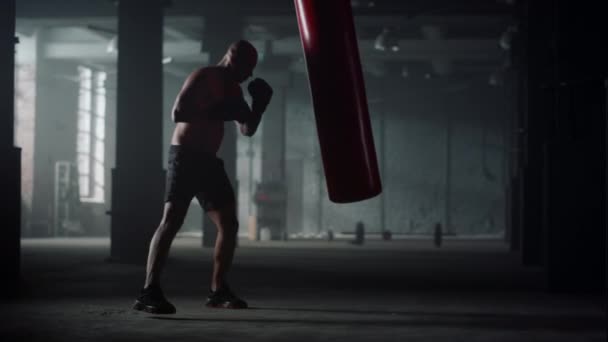 Mann mit muskulösem Körper-Boxsack in Turnhalle. Afro-Typ tritt Sporttasche - Filmmaterial, Video