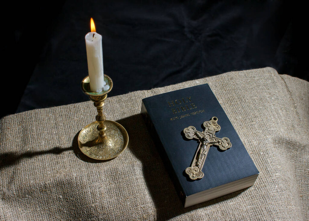 brązowy krzyż, płonąca świeca i Biblia na stole wewnętrzne zbliżenie - Zdjęcie, obraz