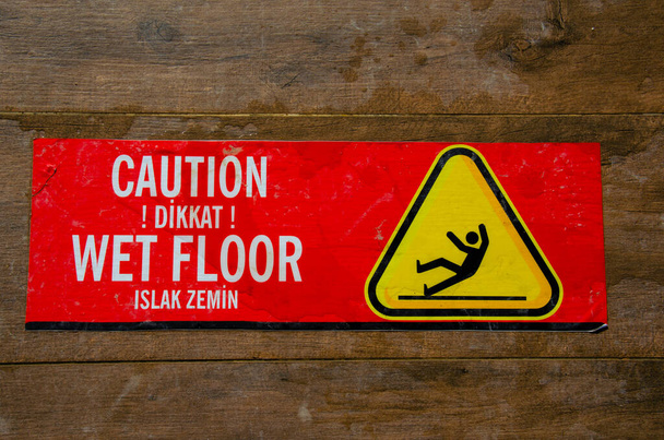 Pegatina de advertencia roja para suelo húmedo en suelo de baldosas marrones. La inscripción en la información roja etiqueta pegajosa precaución piso resbaladizo en el hotel en turco "Dikkat! Islak zemin". - Foto, imagen