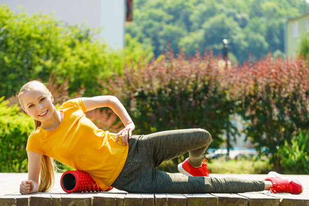 Young woman exercises in park, using gym accessory, foam roller for muscle massage. Staying fit and healthy. - 写真・画像