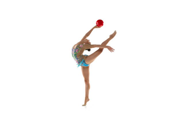 Один молодой гибкий ритмичный гимнаст с красным мячом в движении и действие изолированы на белом фоне студии. - Фото, изображение