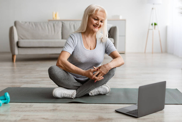 Smiling mature woman exercising on yoga mat using laptop - Foto, Imagen