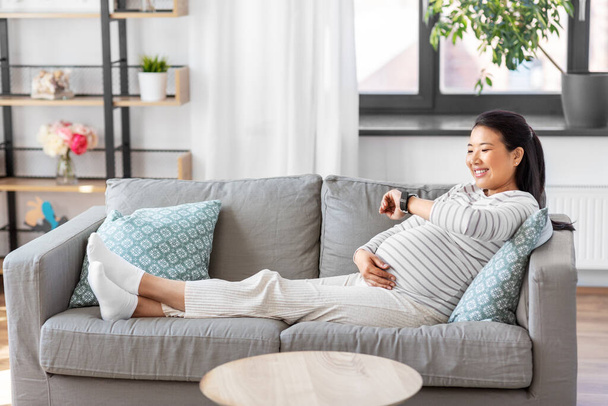 ευτυχισμένη έγκυος γυναίκα με έξυπνο ρολόι στο σπίτι - Φωτογραφία, εικόνα