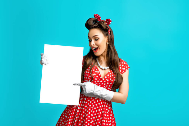 Excited pinup retro style woman pointing at empty advertising banner with copy space on blue studio background, mockup - Foto, Bild
