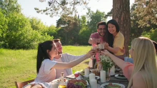 Zeitlupenaufnahmen von glücklichen jungen multiethnischen Menschen, die das Wochenende zusammen auf einer Grillparty verbringen und Gläser mit Getränken klappern - Filmmaterial, Video