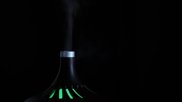 Close up of a stylish air humidifier with nightlight isolated on black background. Concept. Concept of comfort and home style, white steam rising up. - Photo, Image