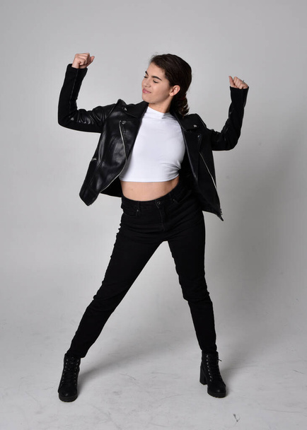 Full length portrait of young woman with natural brown hair,  wearing black leather scifi outfit with jacket, standing pose on light studio background. - Photo, Image