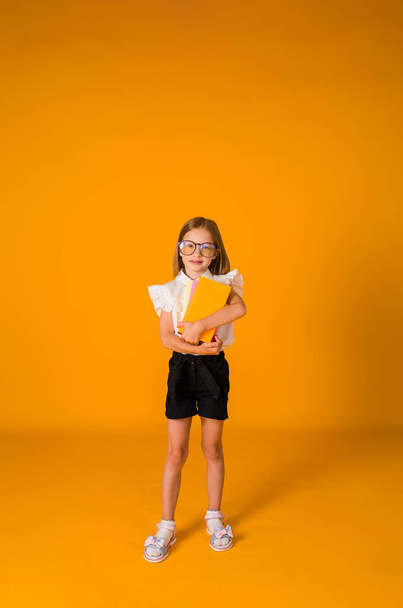 a beautiful schoolgirl in a uniform and glasses holds textbooks on a yellow background with a copy of the space. September 1 - Photo, Image