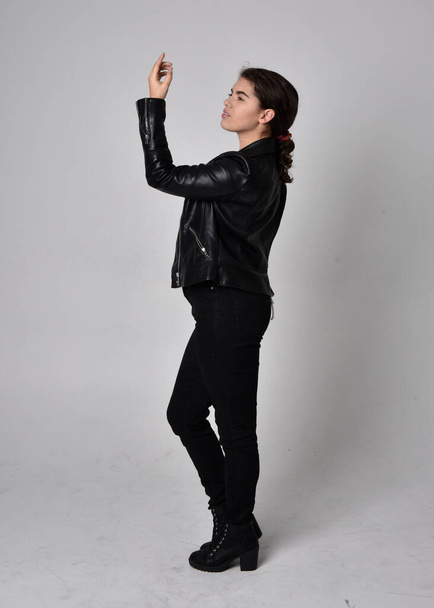 Full length portrait of young woman with natural brown hair,  wearing black leather scifi outfit with jacket, standing pose on light studio background. - Photo, image