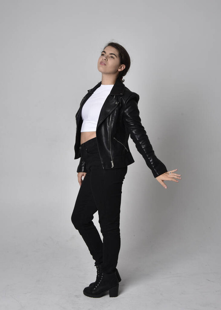 Full length portrait of young woman with natural brown hair,  wearing black leather scifi outfit with jacket, standing pose on light studio background. - Valokuva, kuva