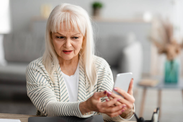 Confused senior woman using her mobile phone - Photo, Image