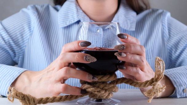 Frauenhände, die ein Weinglas halten, sind mit einem Juteseil gefesselt. Das Konzept der Alkoholabhängigkeit. Das Problem der Behandlung von Alkoholismus - Foto, Bild