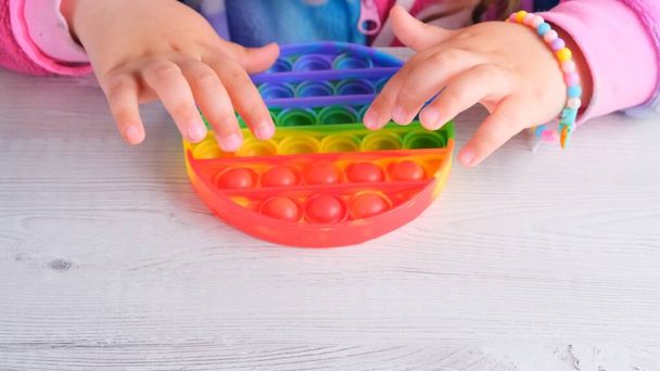 baby female hands playing with pop it sensory toy circle form. little female presses colorful rainbow squishy soft silicone bubbles on white background. Stress and anxiety relief. Trendy fidgeting - Фото, изображение