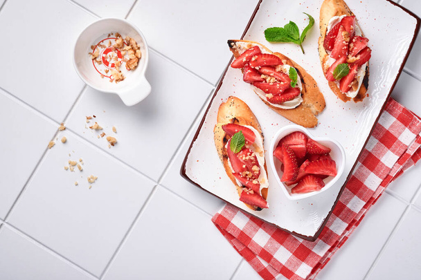 Open sandwiches with strawberries, soft cheese mint and walnut in ceramic plate on a light grey stone background. Summer and healthy dieting food, vegetarian food concept. Top view. - Photo, Image