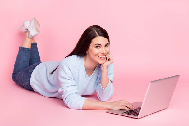 Photo of girlish shiny young lady dressed blue sweater lying floor typing modern device isolated pink color background - Photo, Image